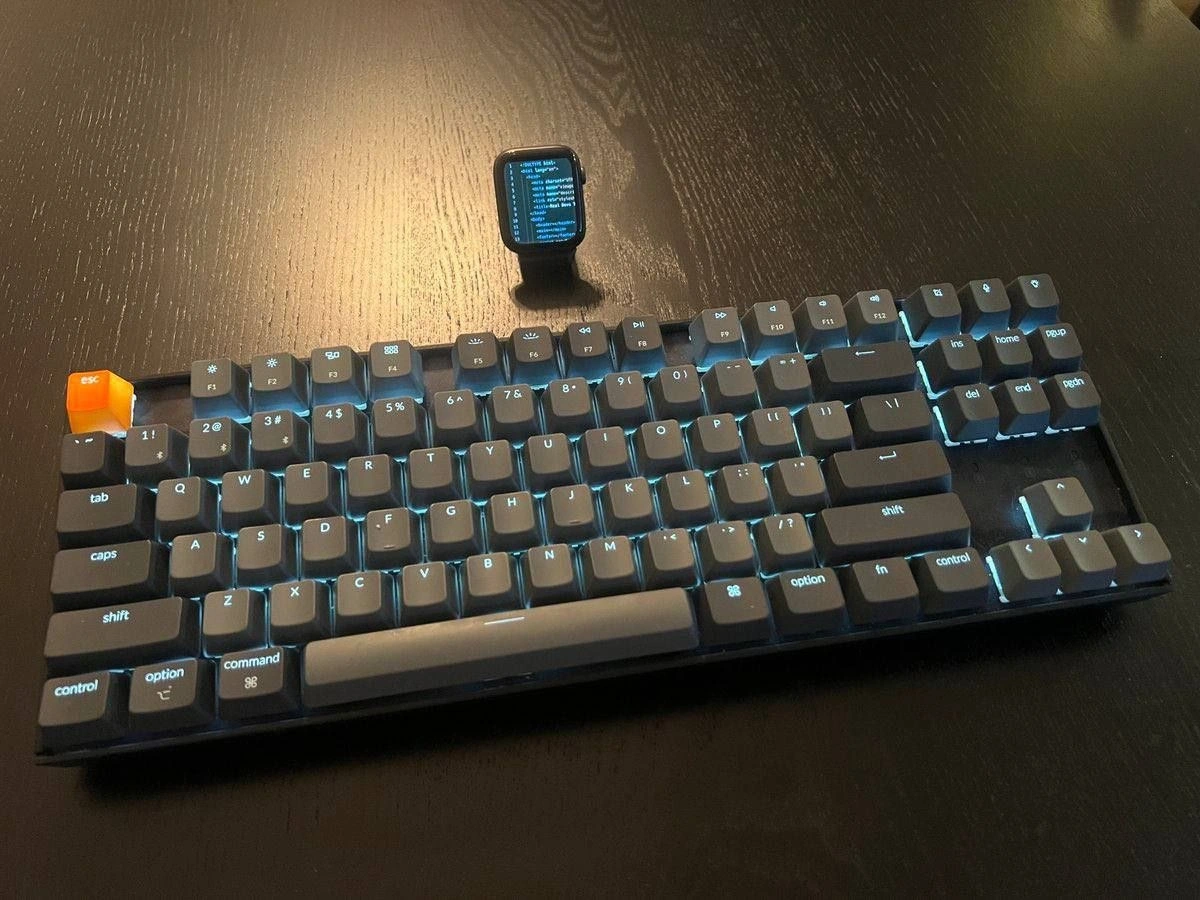 Developer desk flex: glowing keyboard with orange ESC and smartwatch task monitor